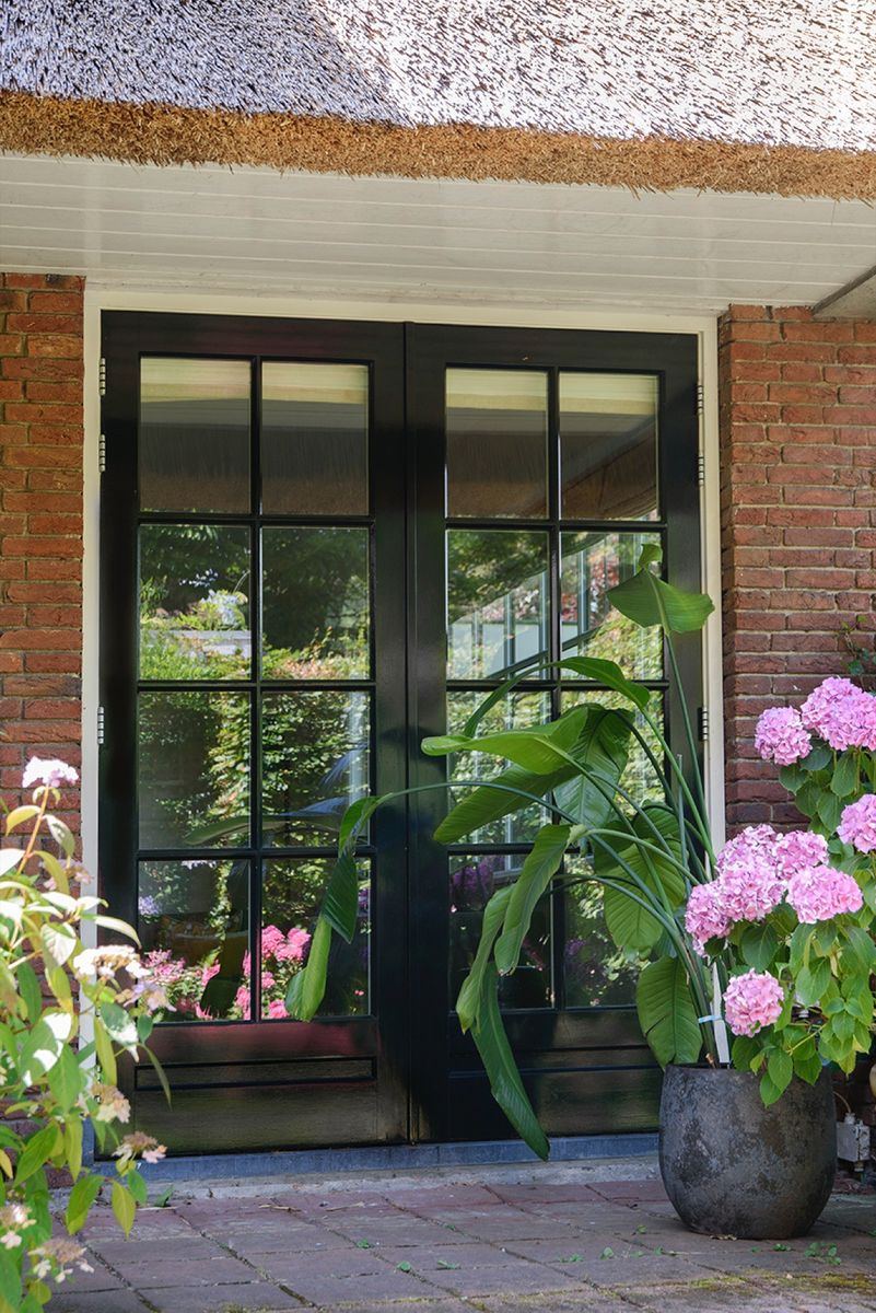 Houten openslaande deuren onder een rieten dak, met hortensia's op het terras